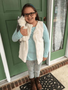 A girl holding a stuffed animal in front of a green door.