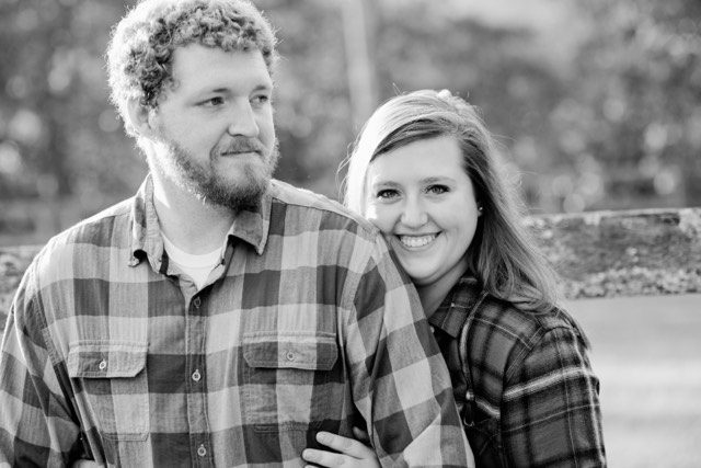 A black and white photo of a couple posing in front of a fence.