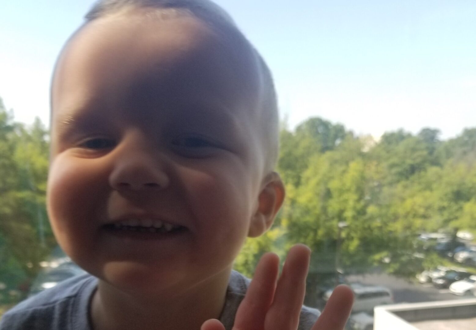 A young boy is making a hand gesture in front of a window.