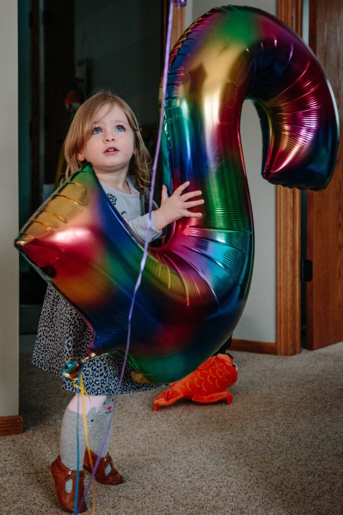 A little girl holding a colorful balloon with the letter s.