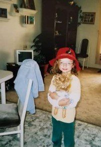 A little girl in a red hat standing in a living room.