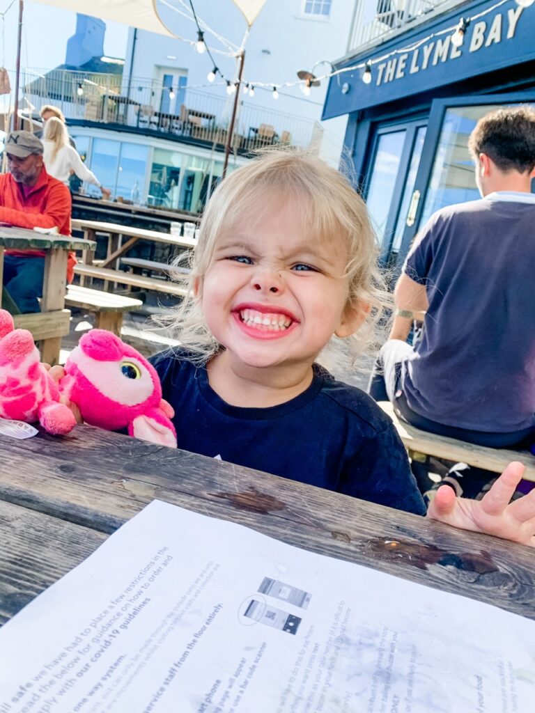 A little girl sitting at a table with a pink teddy bear.