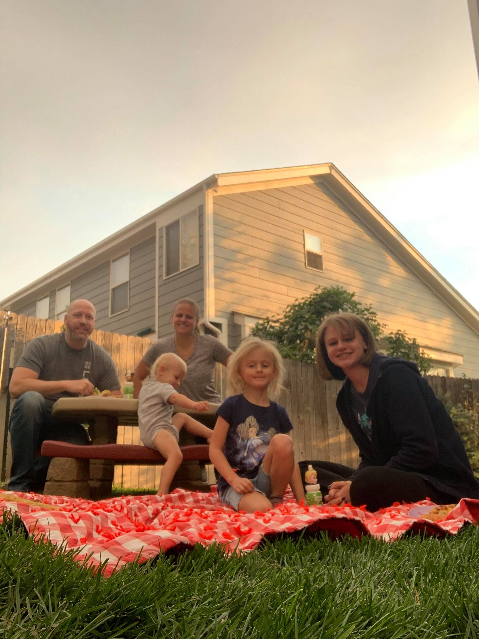 A family sits on a picnic blanket in a backyard.