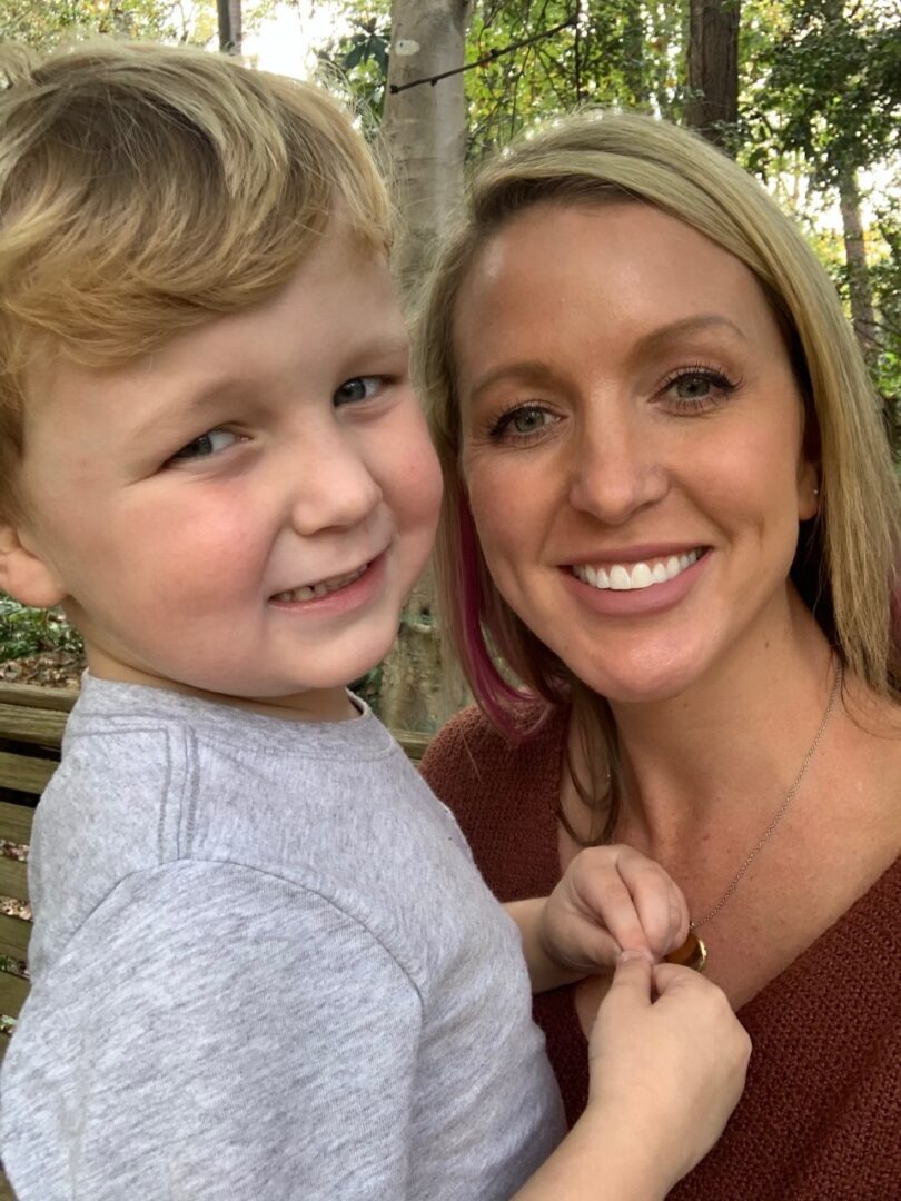 A woman smiles while holding a necklace with a young boy.