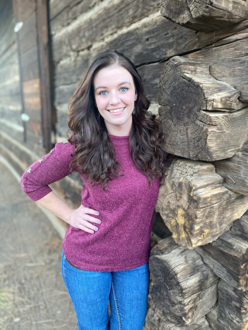 A young woman leaning against a log cabin.