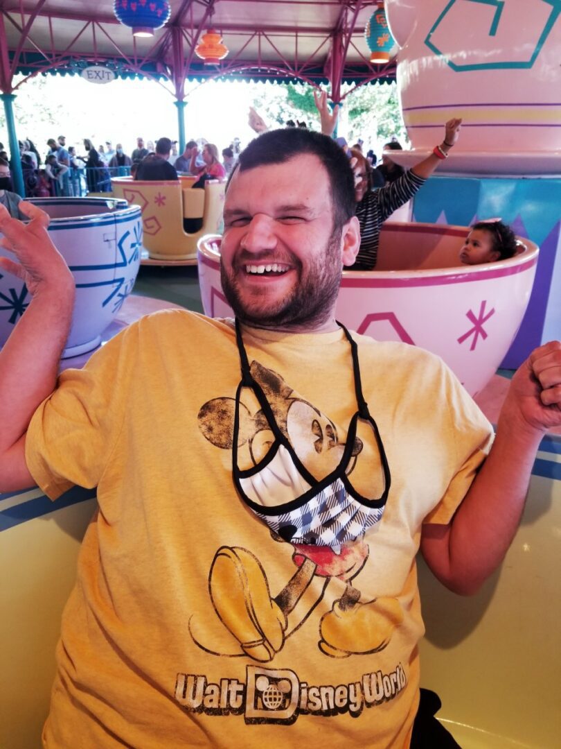 A man in a yellow t - shirt is posing for a picture at disneyland.