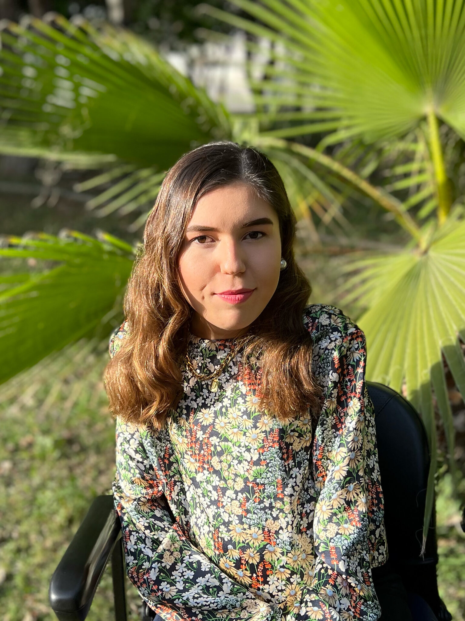 A young woman sitting in a chair in front of a palm tree.