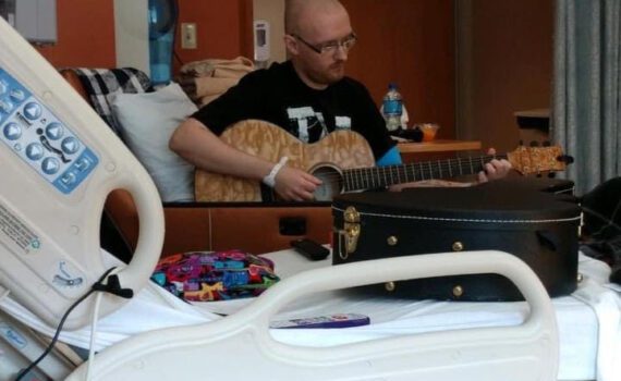 A man playing a guitar in a hospital bed.