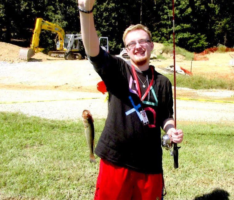 A young man holding up a fish in front of a construction site.