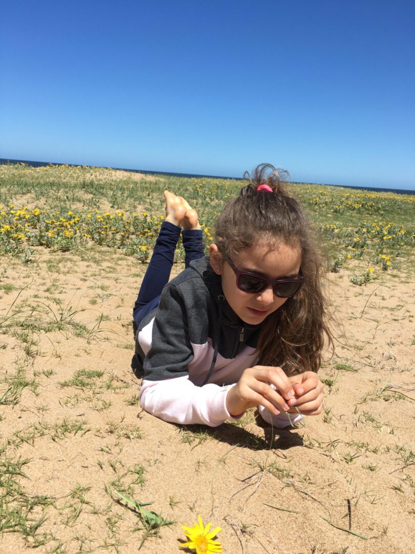 A young girl laying on the sand with a flower in her hand.