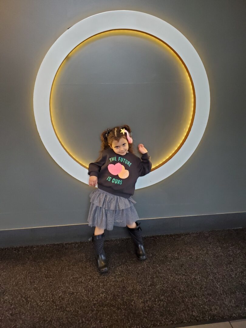 A little girl posing in front of a circular sign for Homocystinuria awareness.