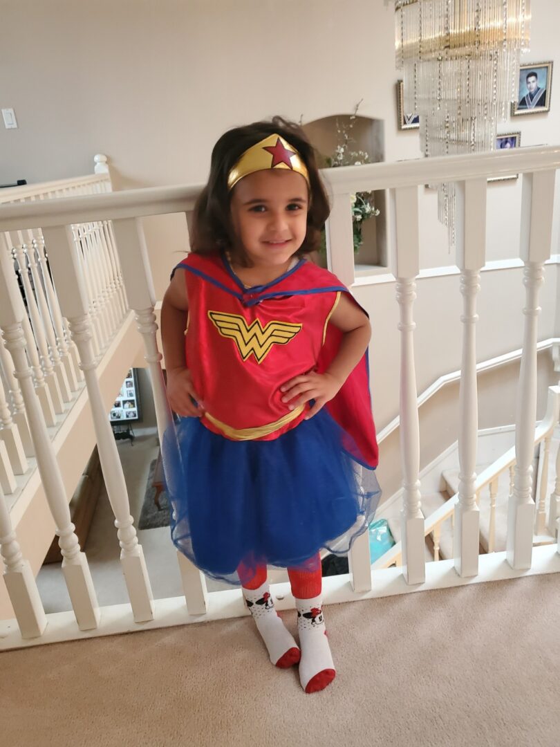 A little girl in a Wonder Woman costume gracefully standing on stairs.