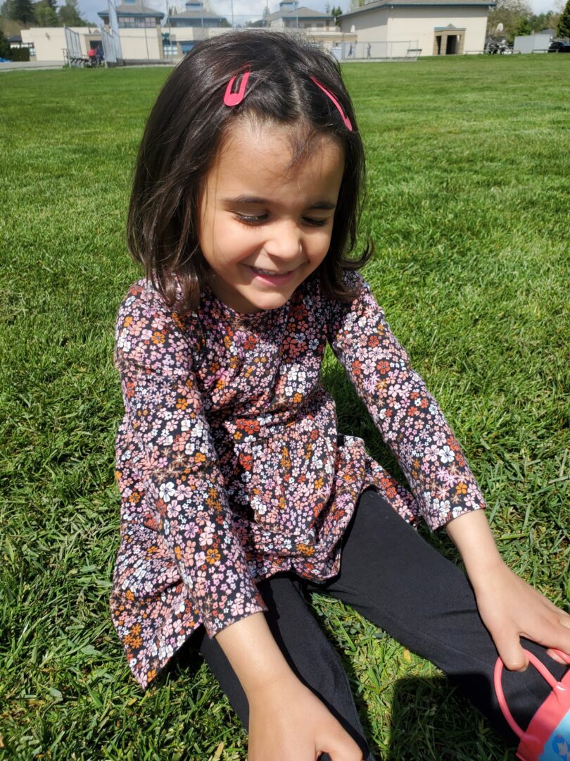 A little girl sitting on the grass with her shoes on, unaffected by Homocystinuria.