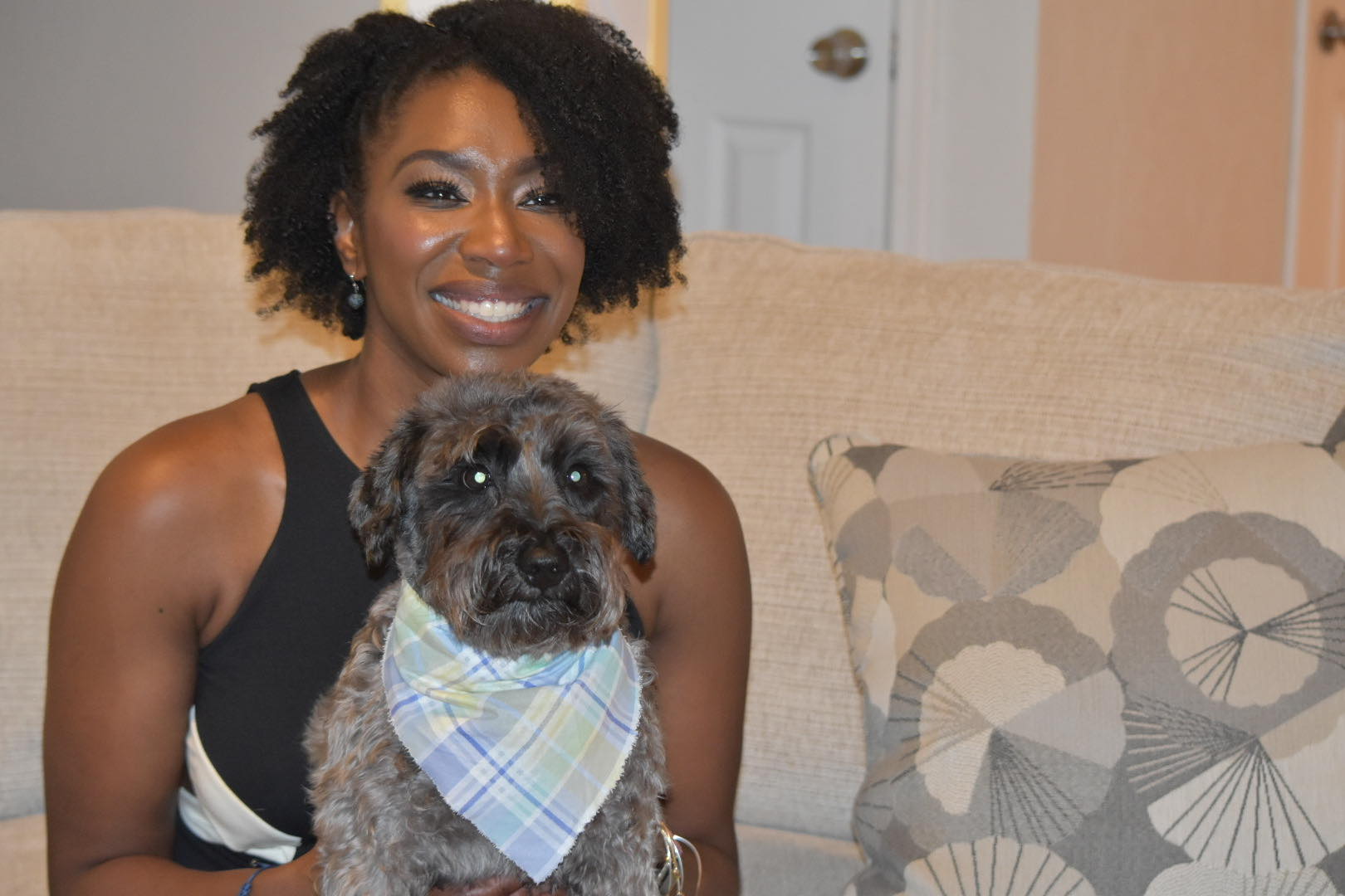 A woman is sitting on a couch with a dog in a bandana.