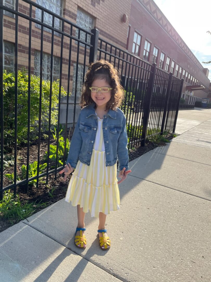 A little girl wearing a denim jacket and yellow striped dress.