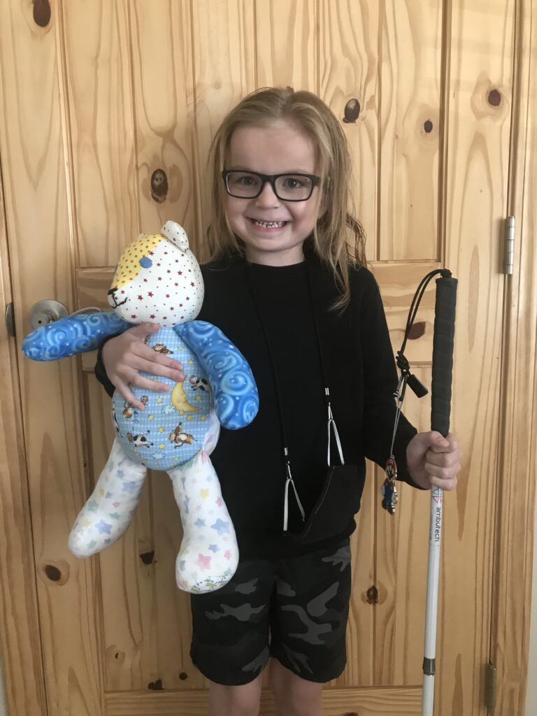 A young girl holding a teddy bear and a cane.