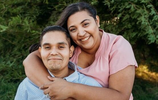 A man and woman hugging in front of a tree.