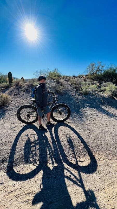 A man standing next to his bike in the desert.