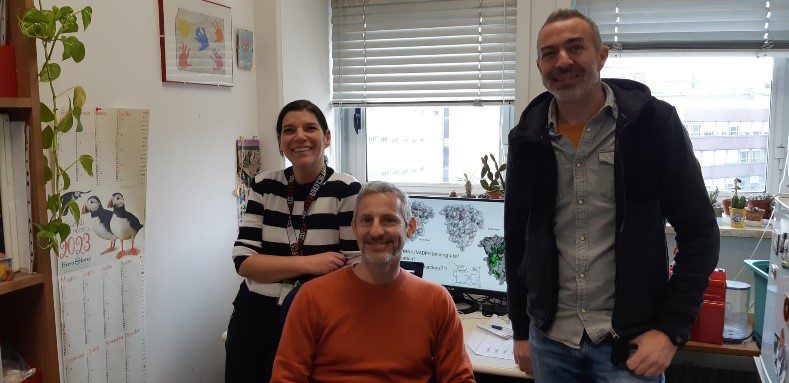 Three people posing in front of a desk in an office.