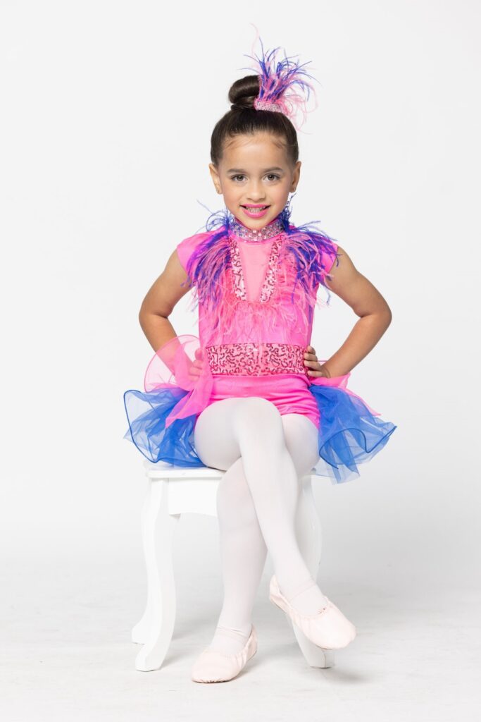 A little girl in a pink and blue tutu posing on a chair.