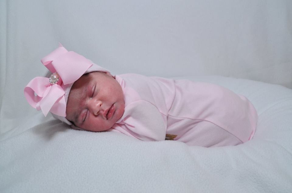 A newborn sleeping on a white pillow with a pink bow.