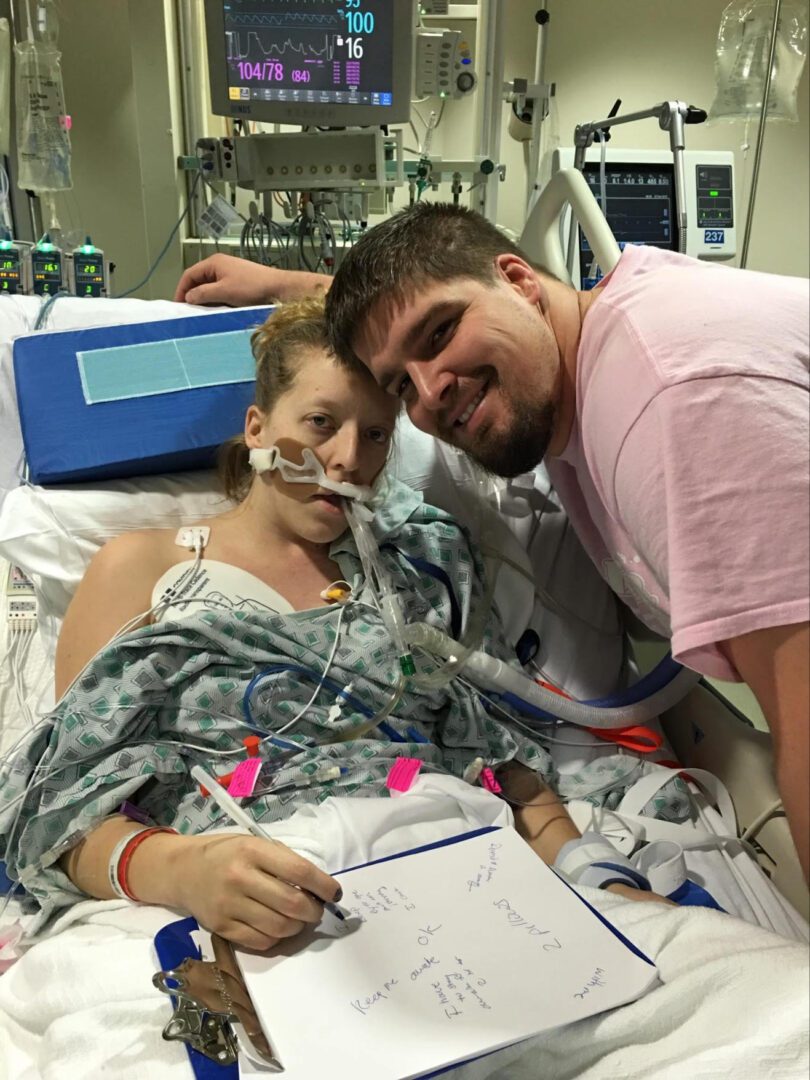 A man in a hospital bed with a woman writing on a piece of paper.