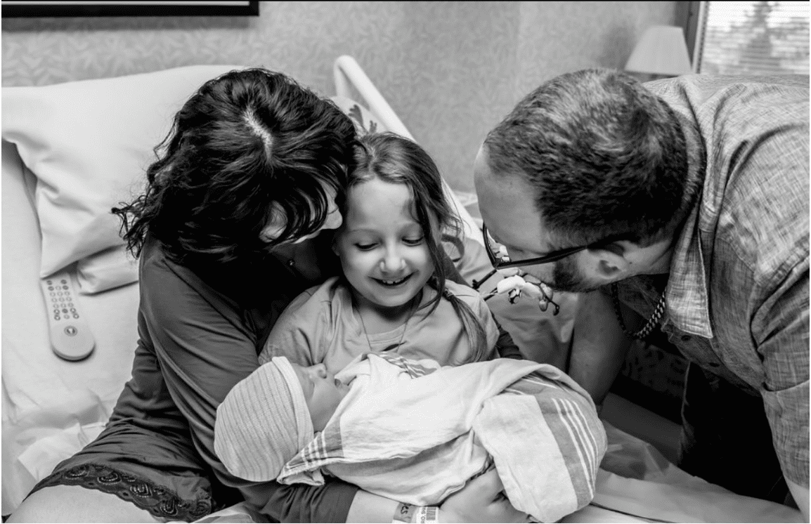 A black and white photo of a family holding a baby in a hospital bed.