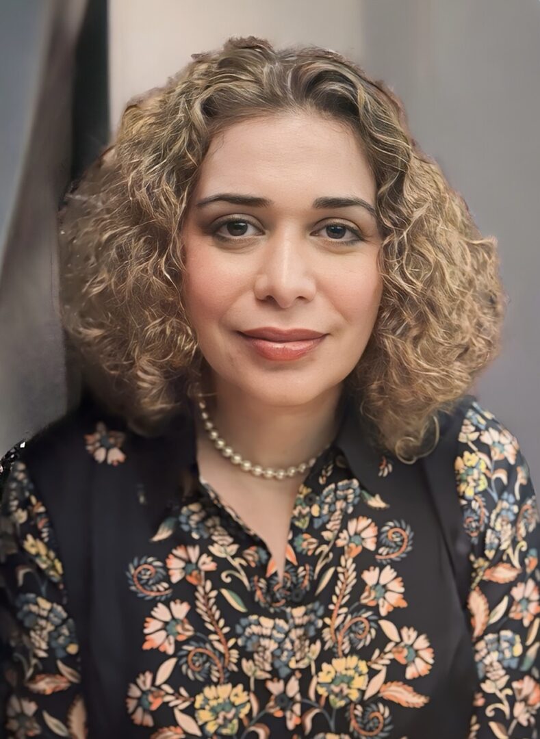 Headshot of a woman with curly hair and a floral shirt.