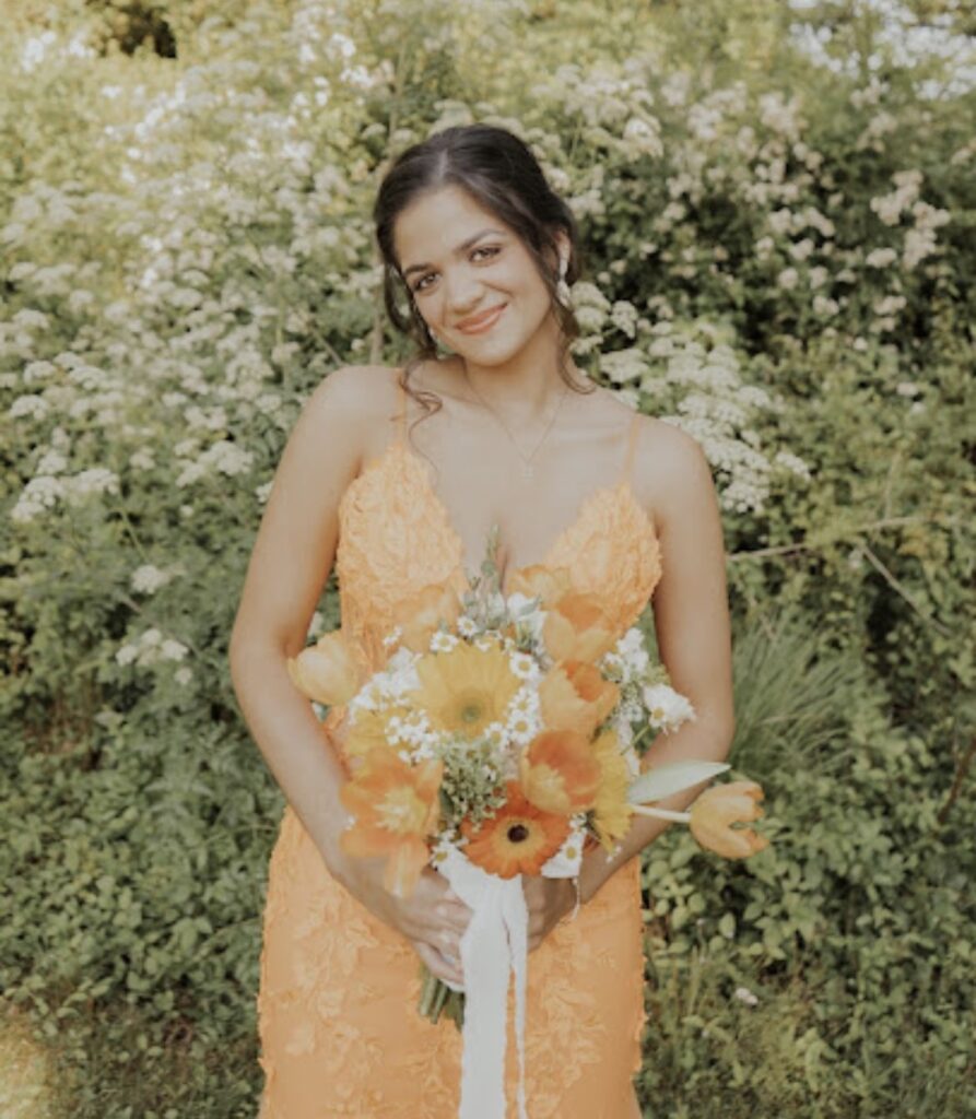 Woman in orange dress holding bouquet of flowers.