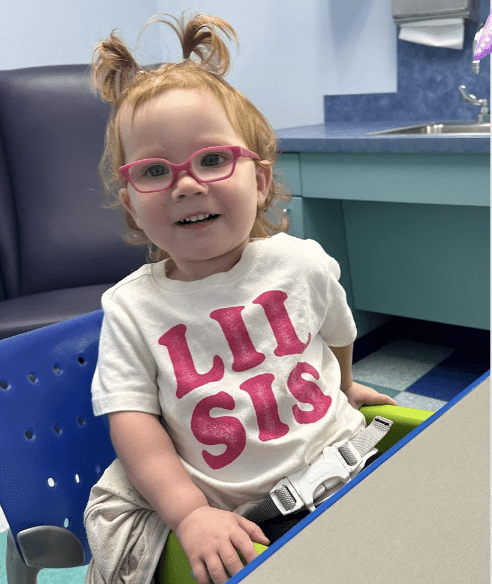 Young girl wearing glasses and "Lil Sis" shirt.