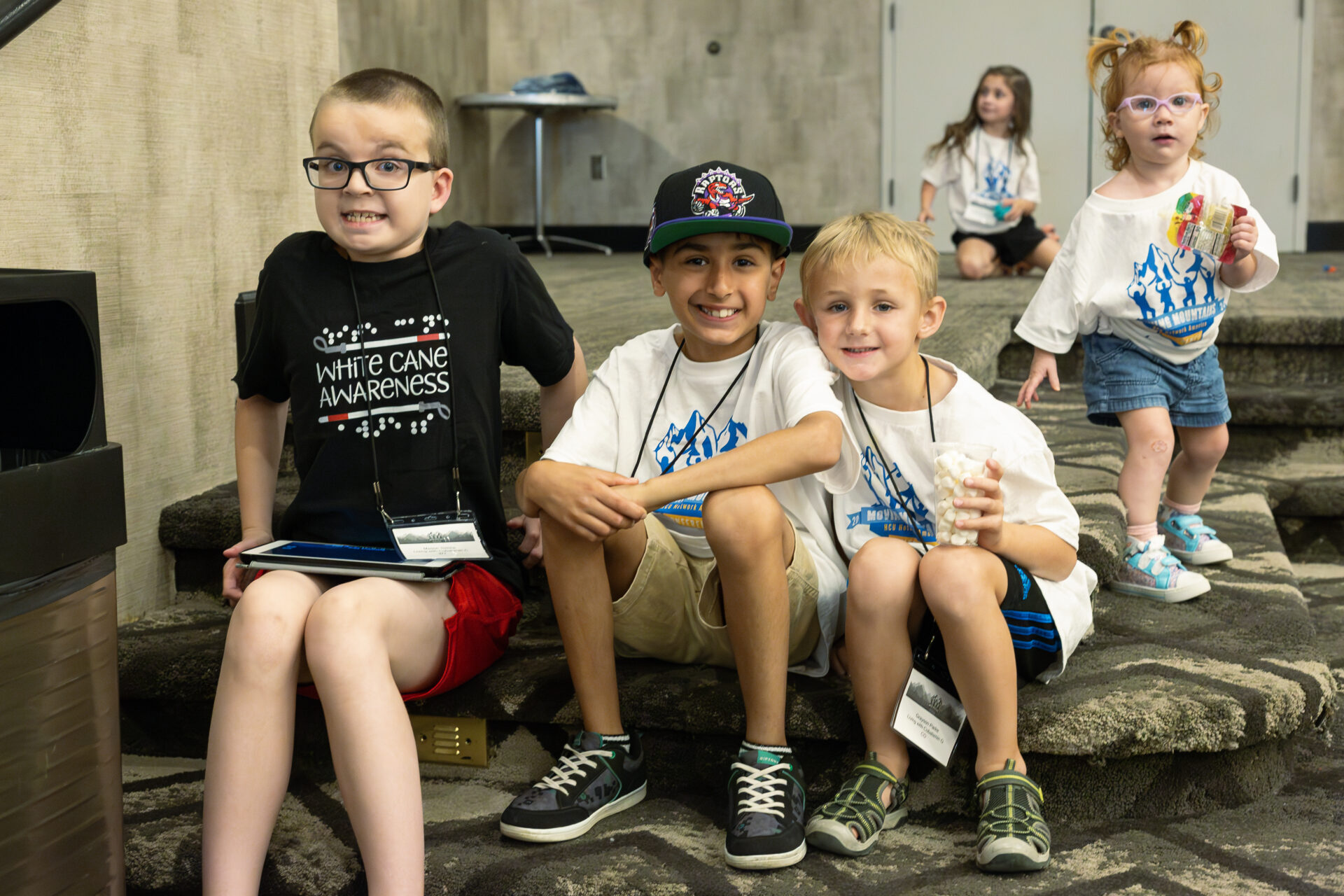 Four kids sitting on stairs, white cane awareness.