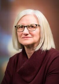 A woman wearing glasses and a maroon sweater.