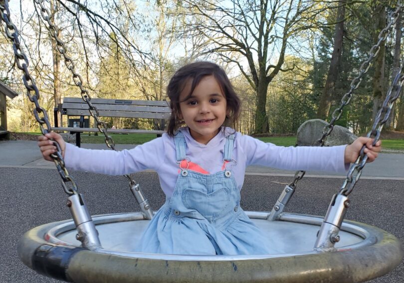 A little girl sitting on a swing in a park.