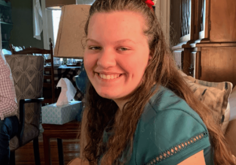 A young woman smiles while sitting in a living room.