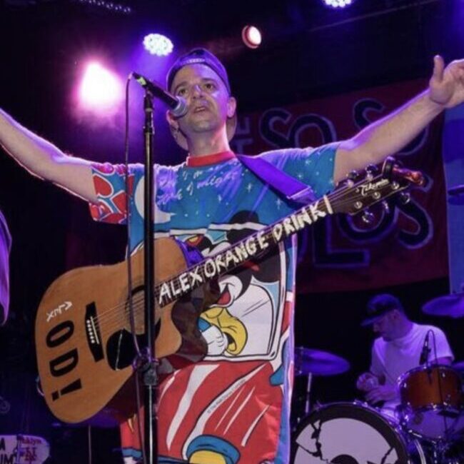 A man with a guitar on stage with his arms outstretched.