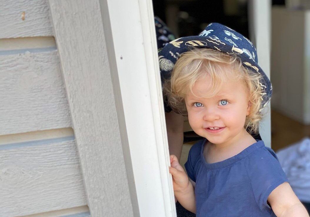 A little girl in a blue hat looking out the door.