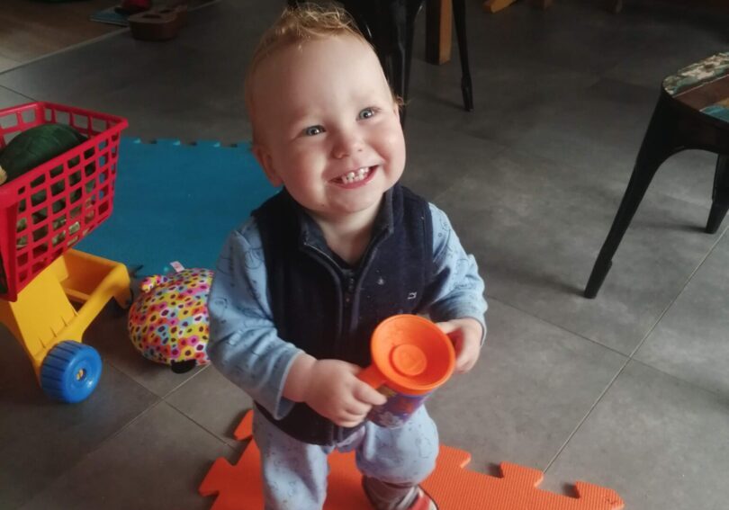 A baby standing on an orange mat with a cup.