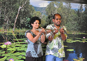 Two people standing in front of a painting of a pond.