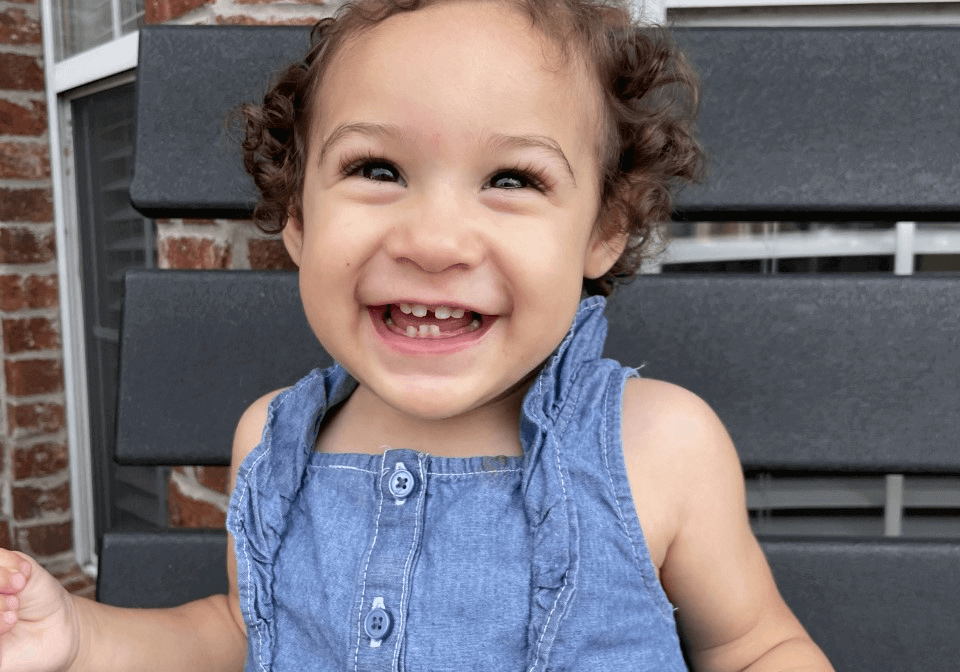 A little girl is smiling while sitting on a bench.