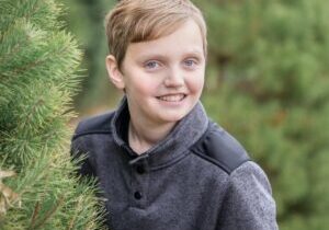 A boy smiles while leaning against a christmas tree.