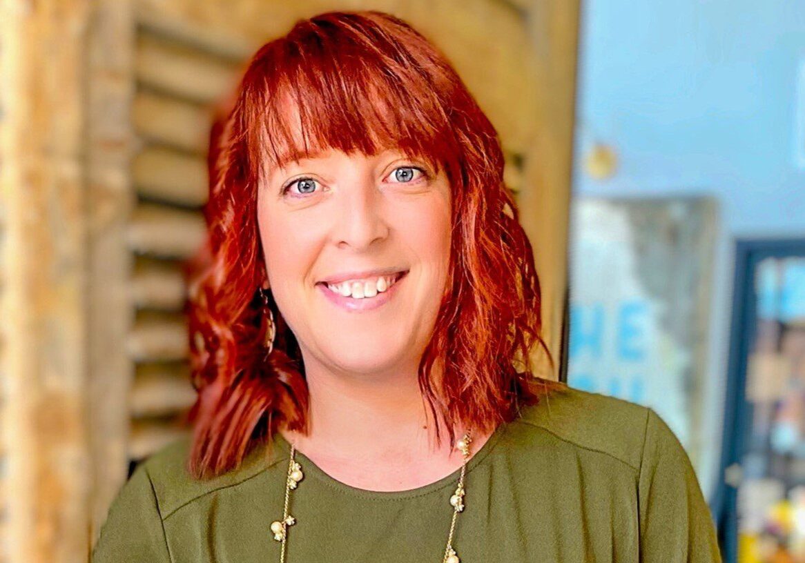 A woman with red hair smiling in front of a building.