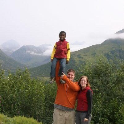 A man, woman and child standing on a road with mountains in the background.