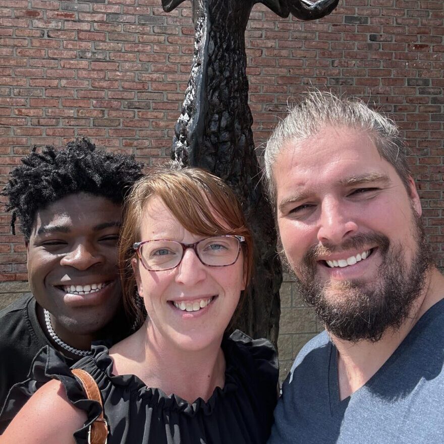 Three people posing for a photo in front of a deer statue.