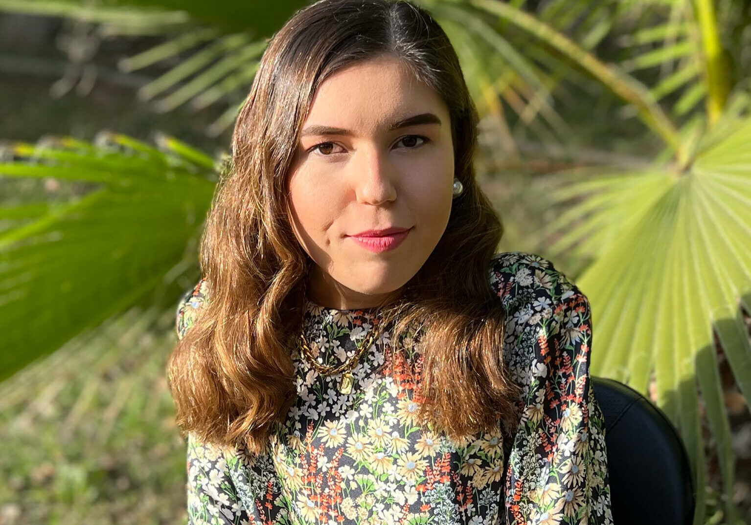 A young woman sitting in a chair in front of a palm tree.