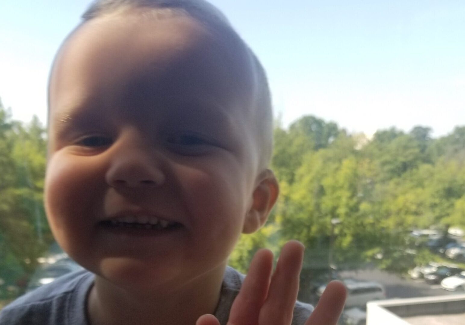 A young boy is making a hand gesture in front of a window.