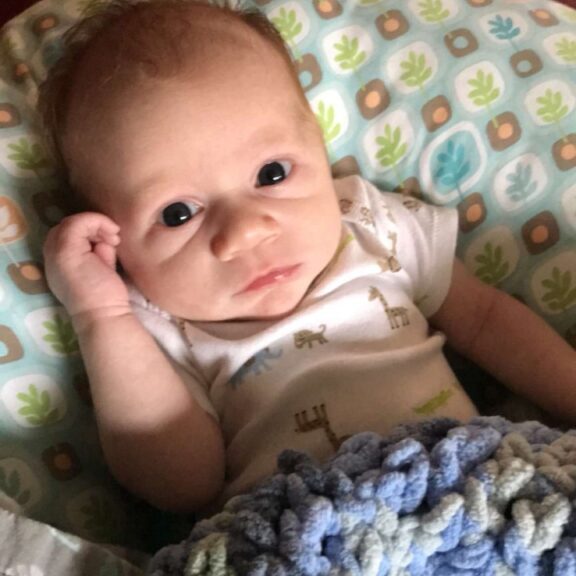 A baby in a blue blanket laying on a bed.