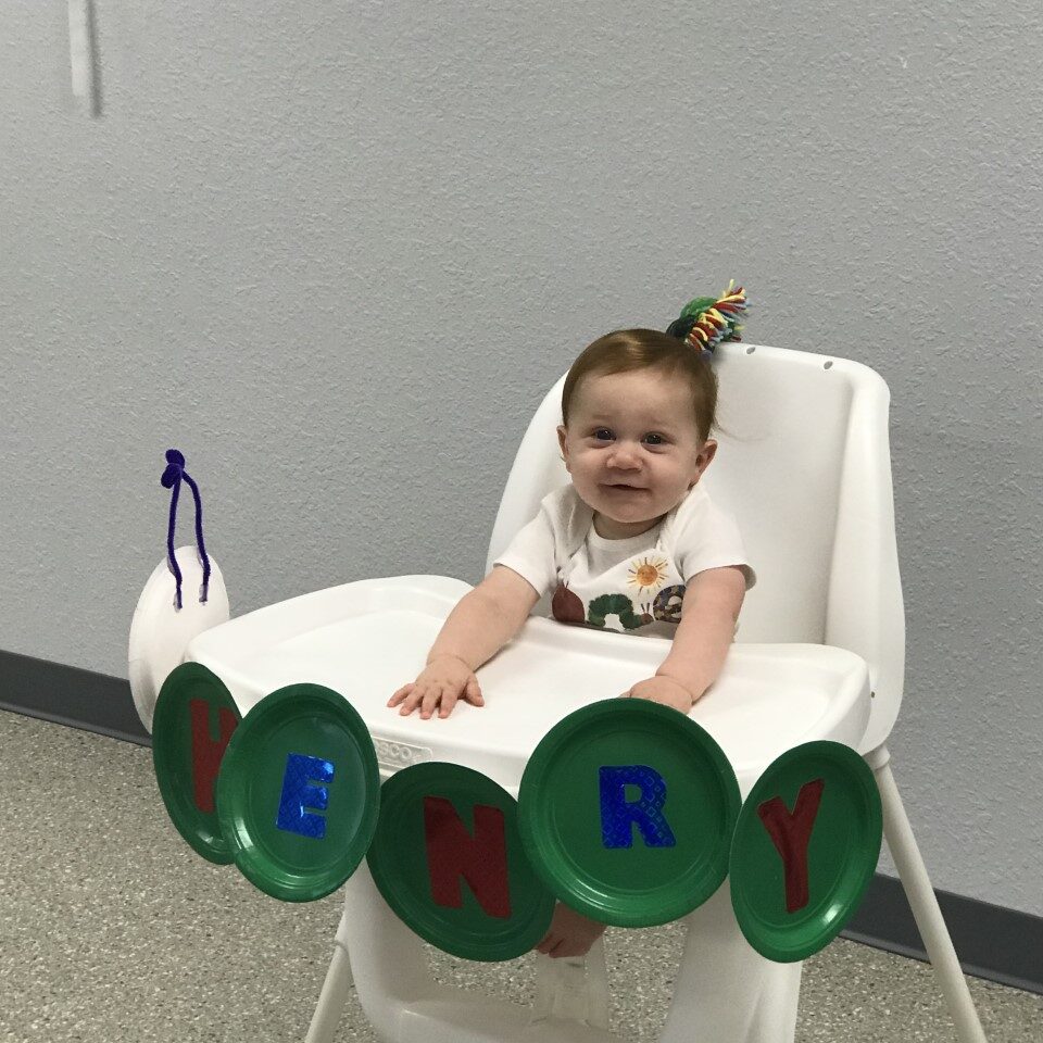 A baby sitting in a high chair with a caterpillar on it.