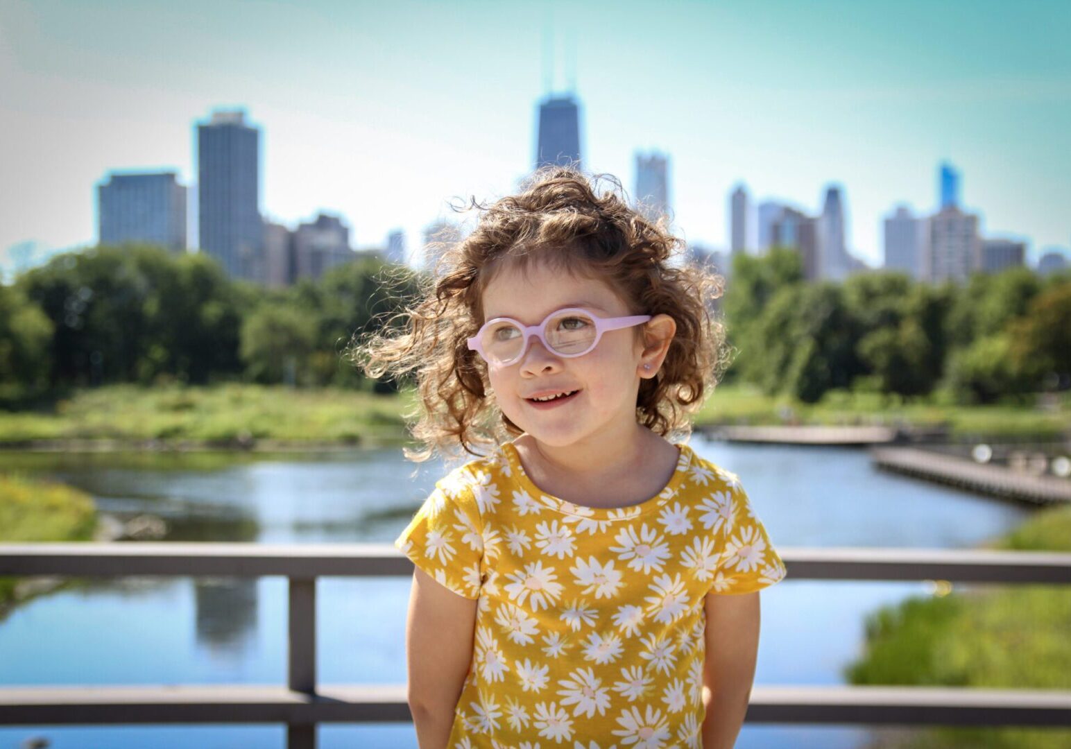 A little girl wearing glasses in front of a city skyline.