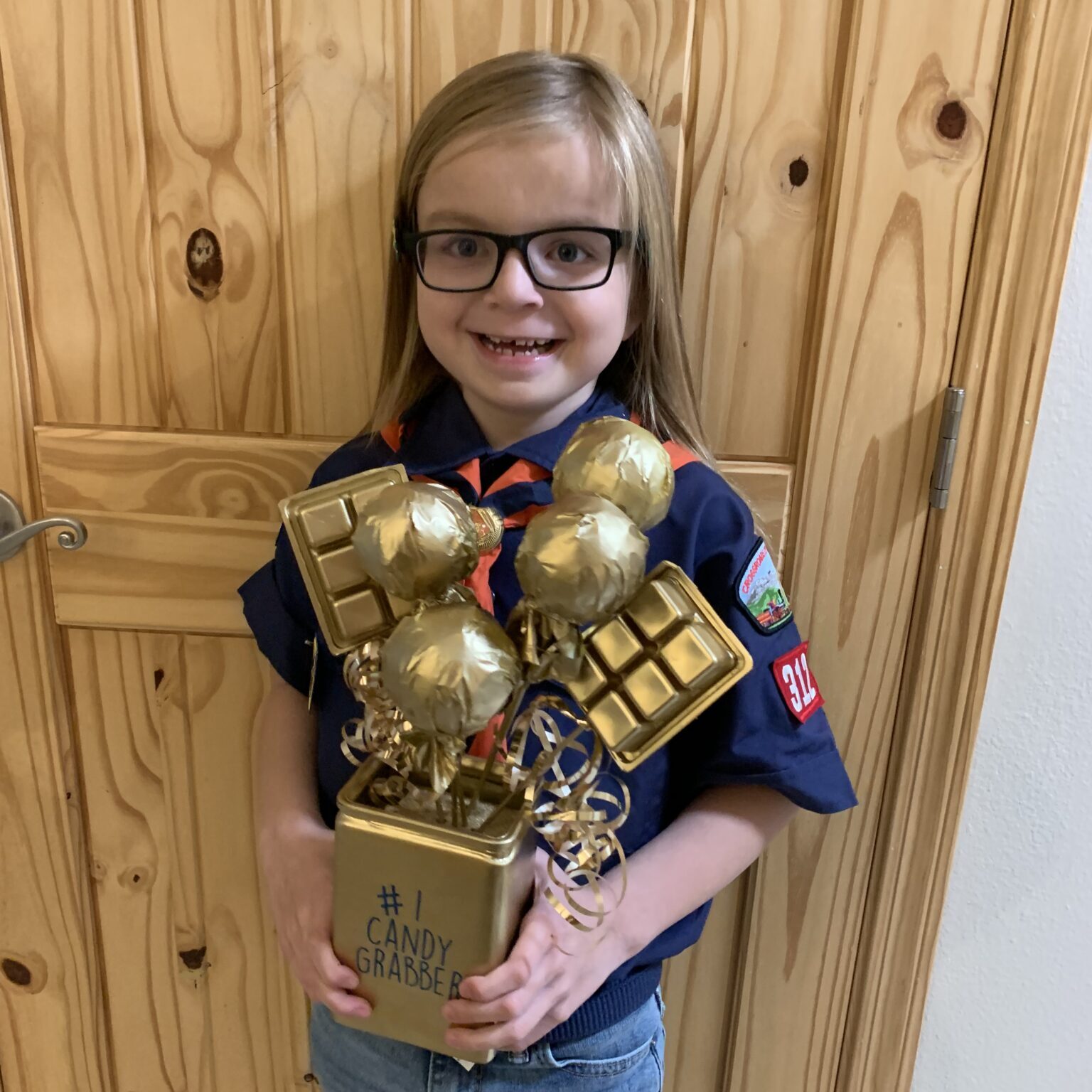 A girl in glasses holding a gold scout award.