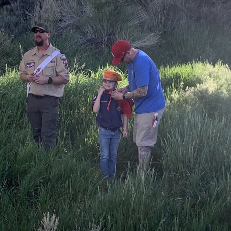 Three scouts standing next to a boy in the grass.